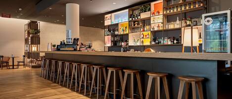 Un espace bar avec des tabourets en bois, un comptoir où sont exposées différentes bouteilles et un appareil à café.