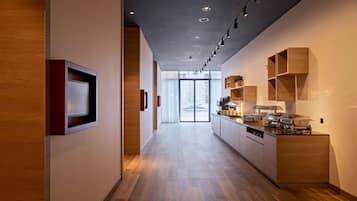 Un pasillo moderno de hotel con piso de madera, iluminación empotrada y una zona de cocina con gabinetes de madera y encimera.