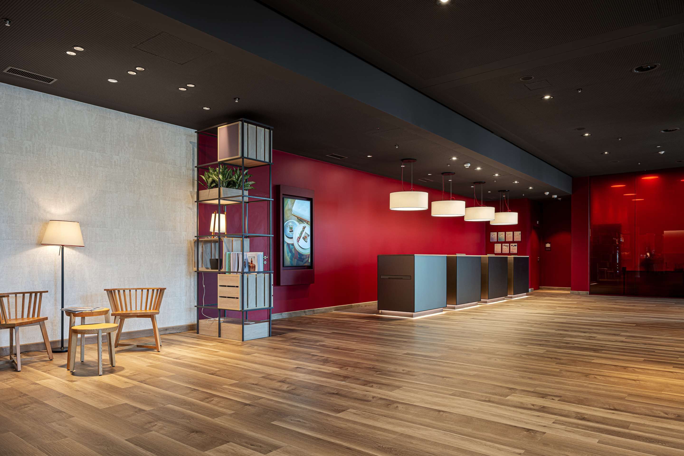 A spacious lobby with wooden flooring, a reception desk, and a modern shelving unit with plants.