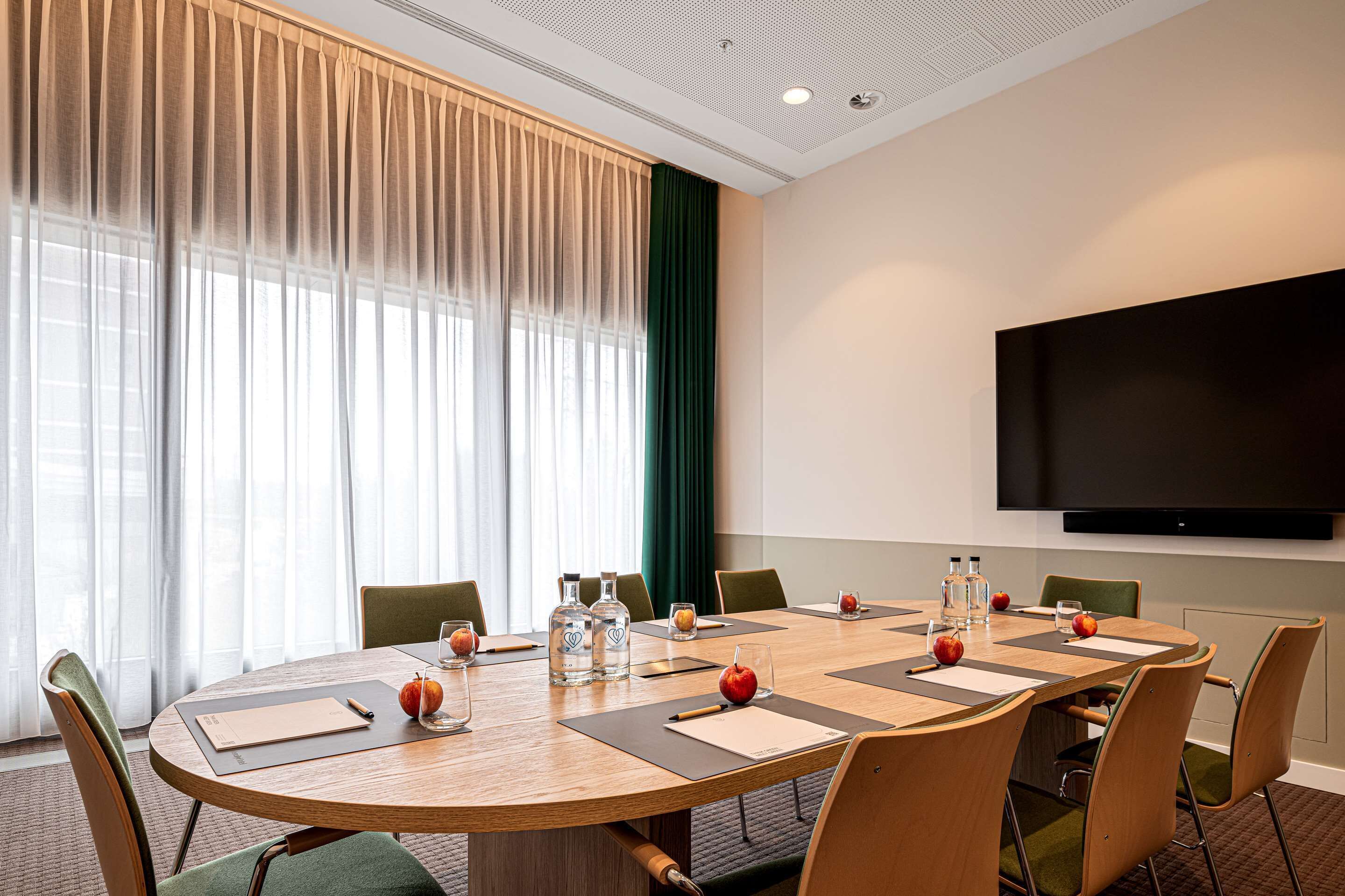 A conference room with a large table, chairs, a flat-screen TV, and a window with curtains.