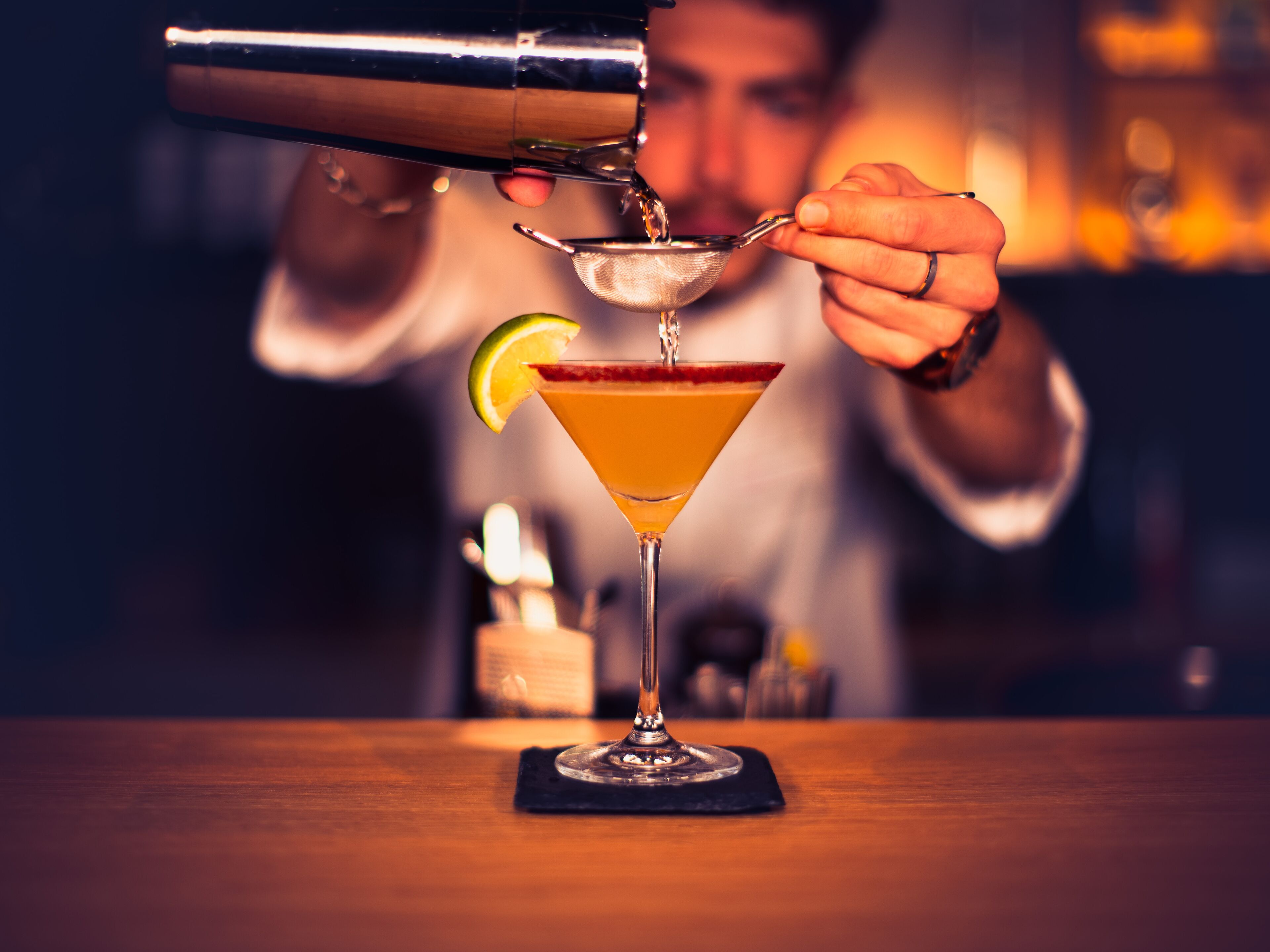 A bartender pouring a drink into a martini glass with a lime wedge on the rim.