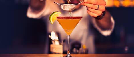 A bartender pouring a drink into a martini glass with a lime wedge on the rim.