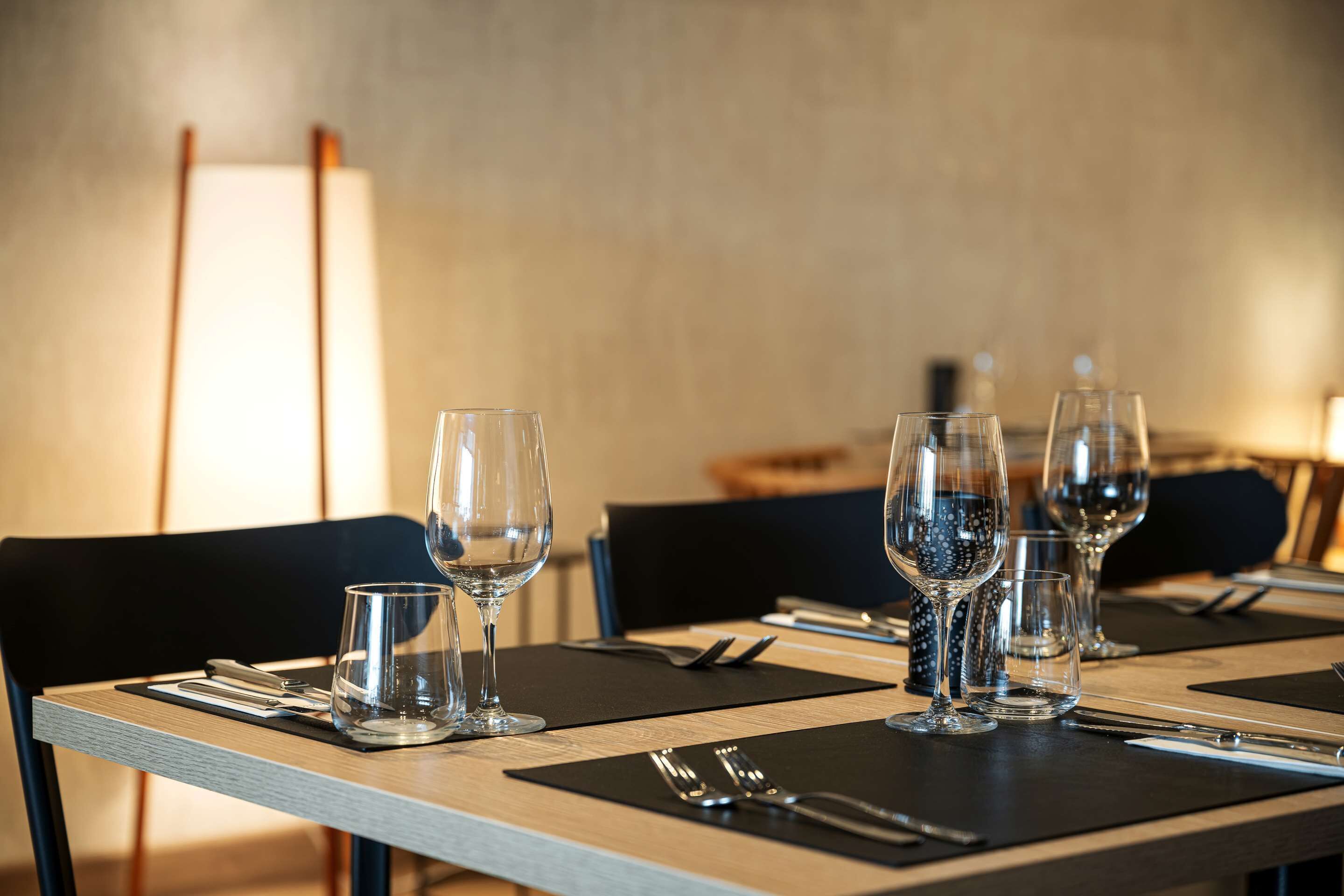 Una mesa de comedor con copas de vino, cubiertos y manteles individuales negros.