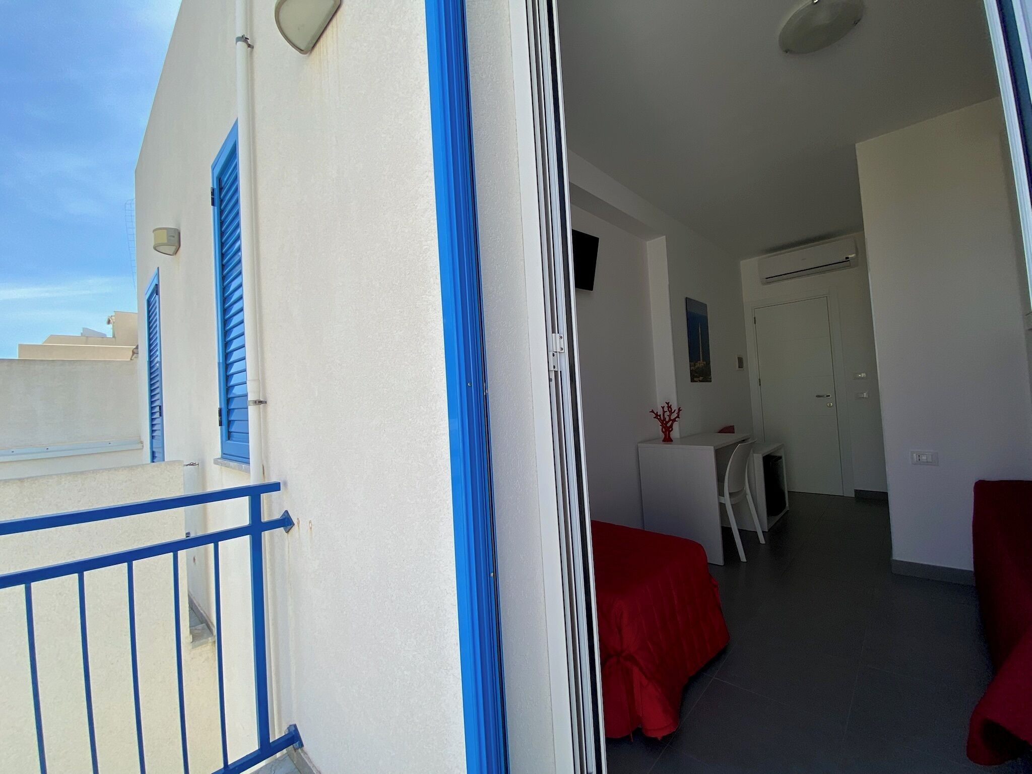 A room with a balcony, a desk, a chair, and a bed.