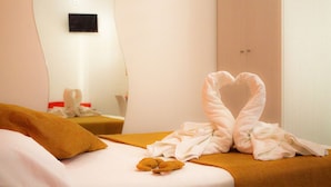 Una habitación de hotel con una cama, una toalla dispuesta en forma de corazón y un osito de peluche sobre la cama.