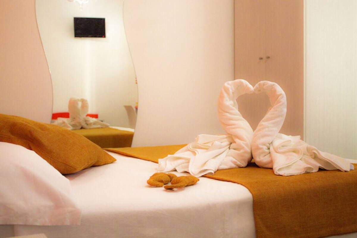 Une chambre d’hôtel avec un lit, une serviette pliée en forme de cœur et un ours en peluche posé sur le lit.