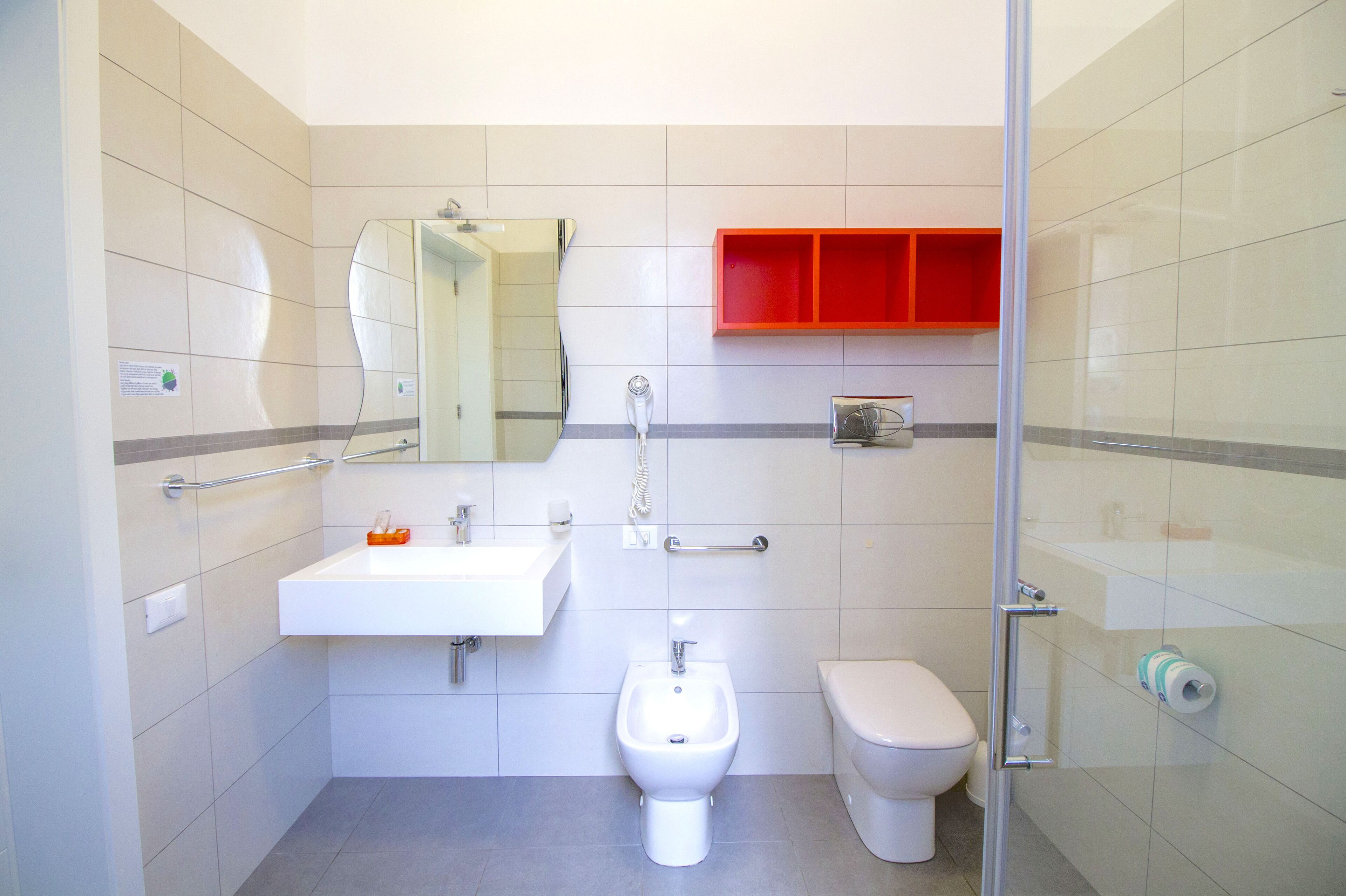 A modern bathroom with a white sink, bidet, toilet, and a glass shower enclosure.
