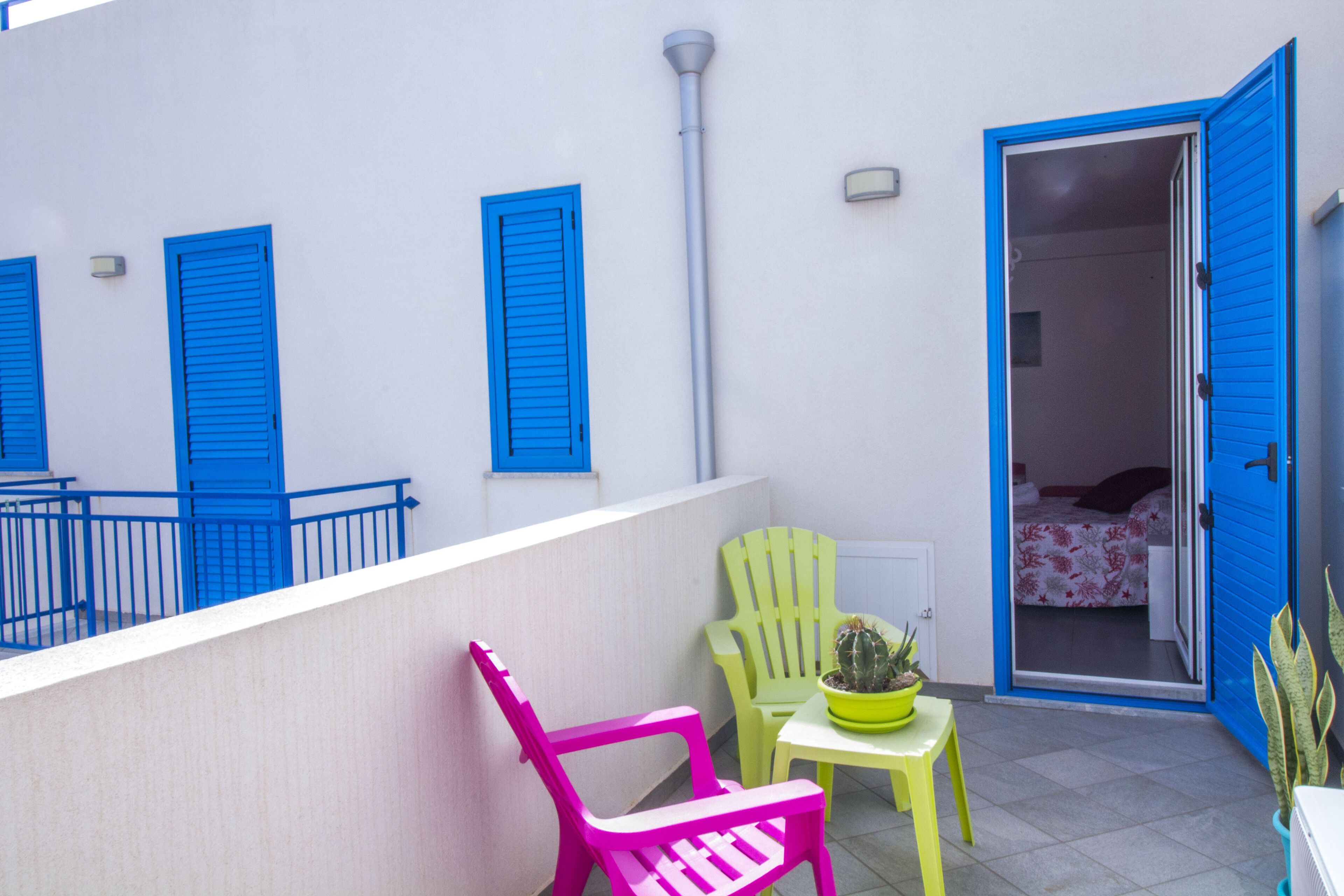 Een balkon met blauwe luiken, een cactus in een pot en twee stoelen.