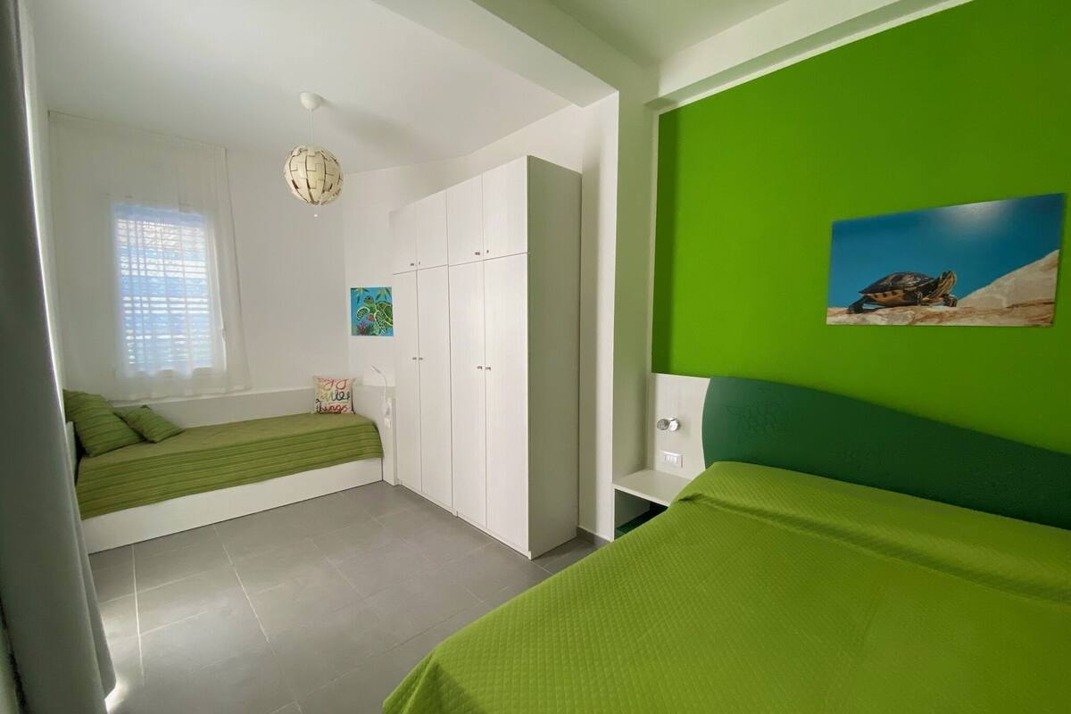 Une chambre avec un lit, une armoire, un bureau et un mur vert orné d’un tableau représentant une tortue.