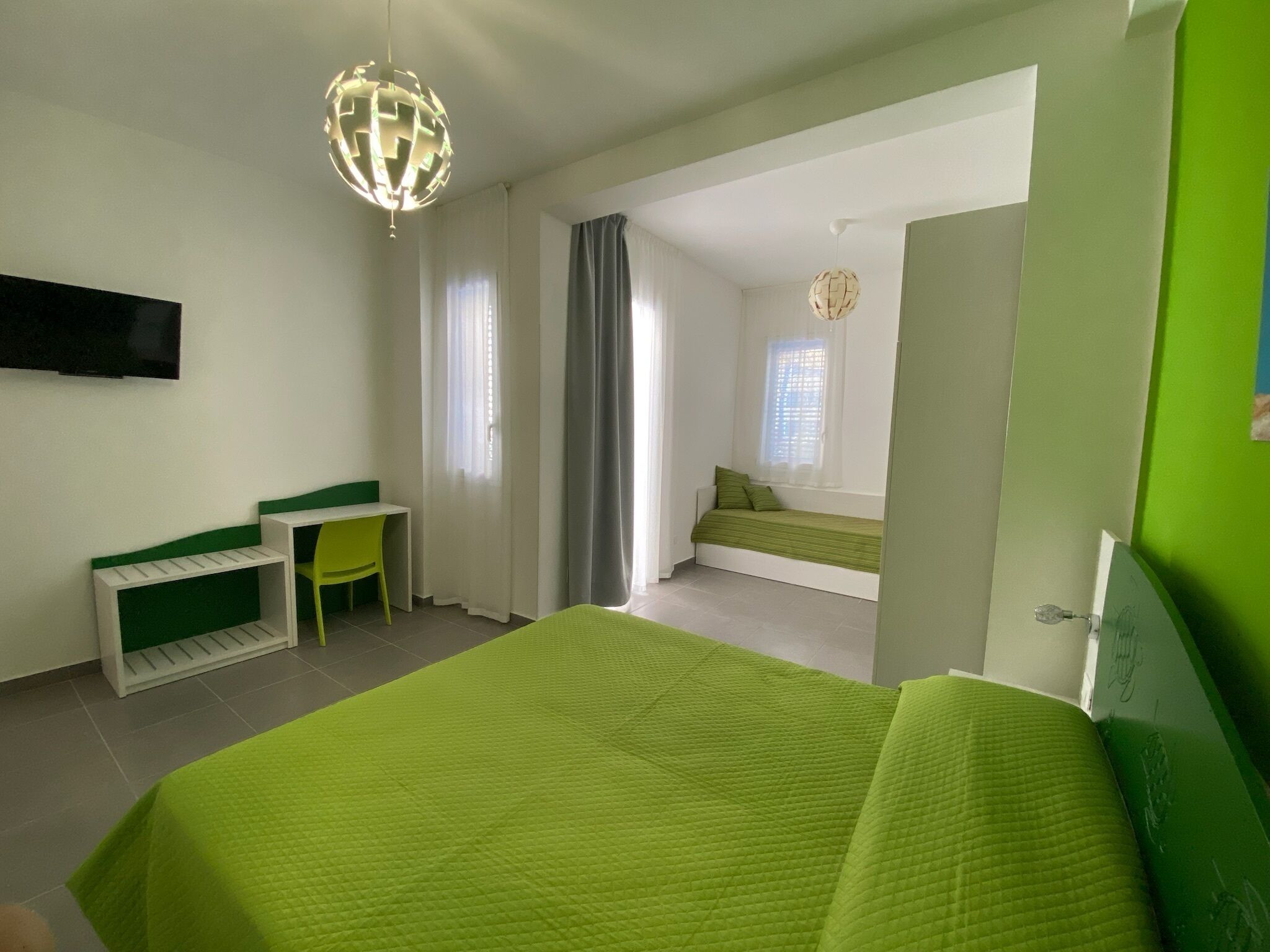 Un dormitorio con cama, escritorio, silla, ventana y puerta.