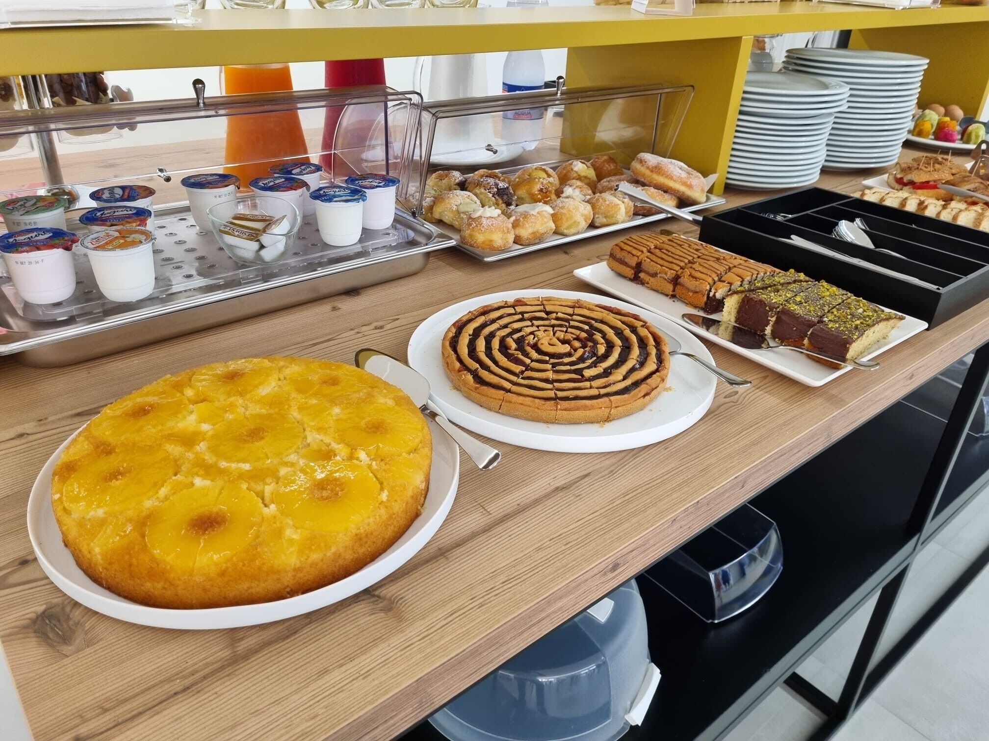 A buffet with various desserts including a pineapple cake, a spiral cake, and a chocolate cake with pistachios.