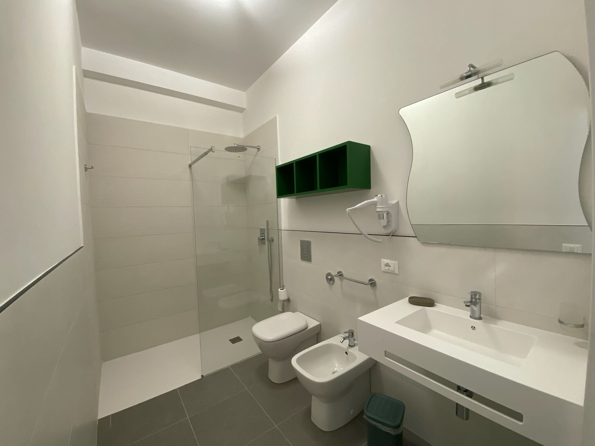 A modern bathroom with a shower, toilet, bidet, sink, and a green medicine cabinet.