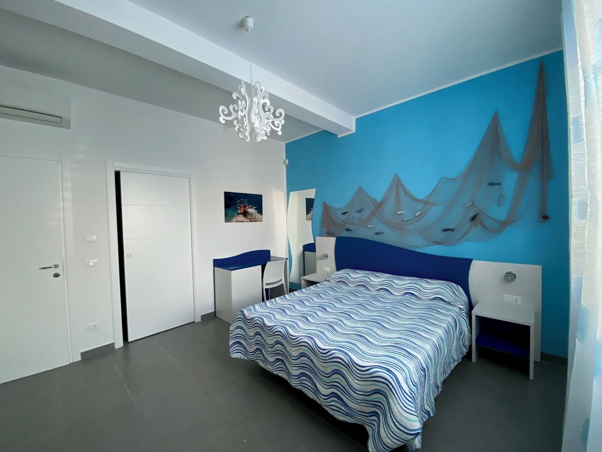 A bedroom with a bed, a desk, a chair, a wall-mounted artwork, and a ceiling light fixture.