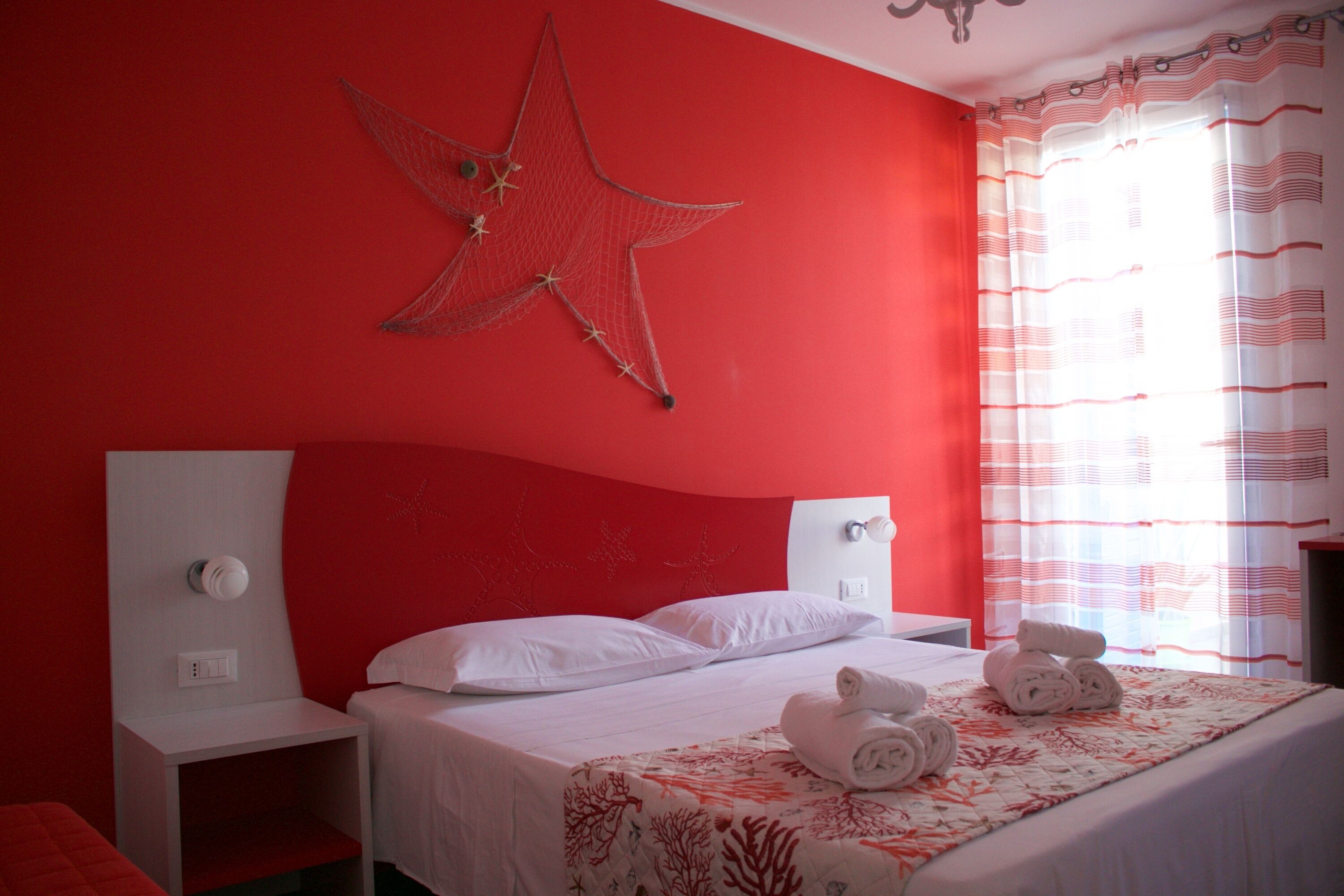 Un dormitorio con paredes rojas, una cama y un cabecero blanco, además de una decoración con motivos de estrellas.