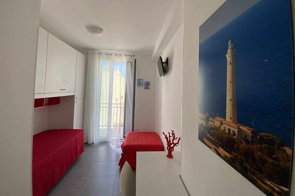 Une chambre avec un lit, un bureau, une télévision et un tableau représentant un phare.