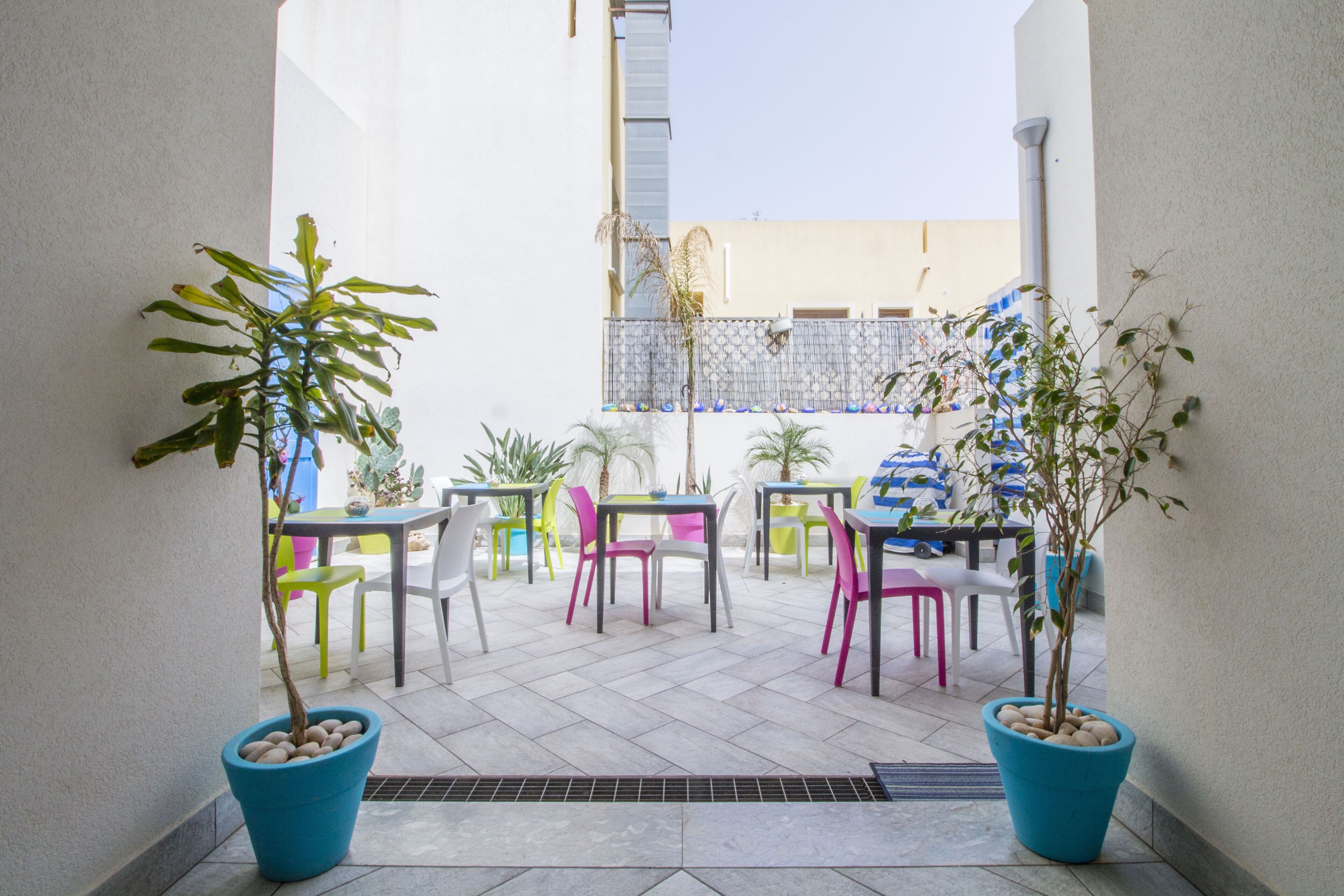 An outdoor patio area with tables and chairs, potted plants, and a view of the street.