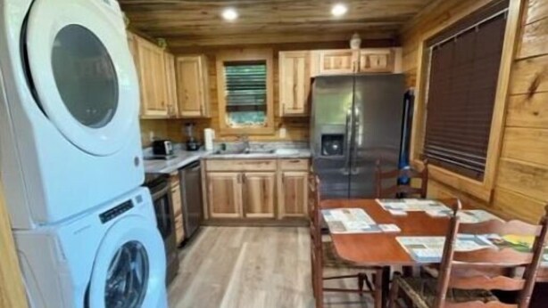 Una cocina compacta con armarios de madera, lavadora, refrigerador y una mesa de comedor con sillas.