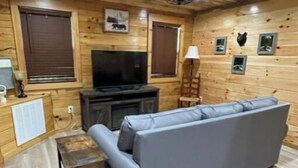 A wooden cabin interior with a sofa, a television, and a ceiling fan.