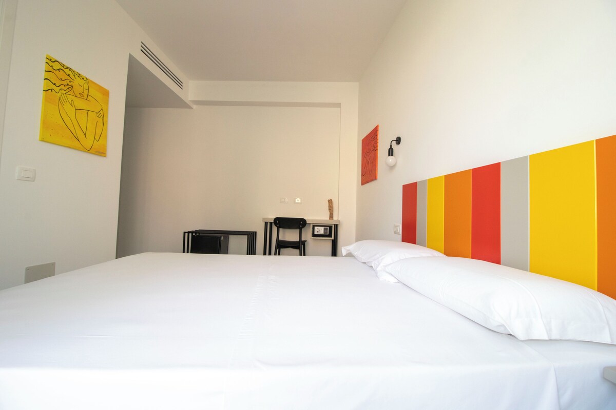 Een hotelkamer met een groot bed, een bureau en een stoel. Er hangt een schilderij aan de muur en een lamp boven het bureau.