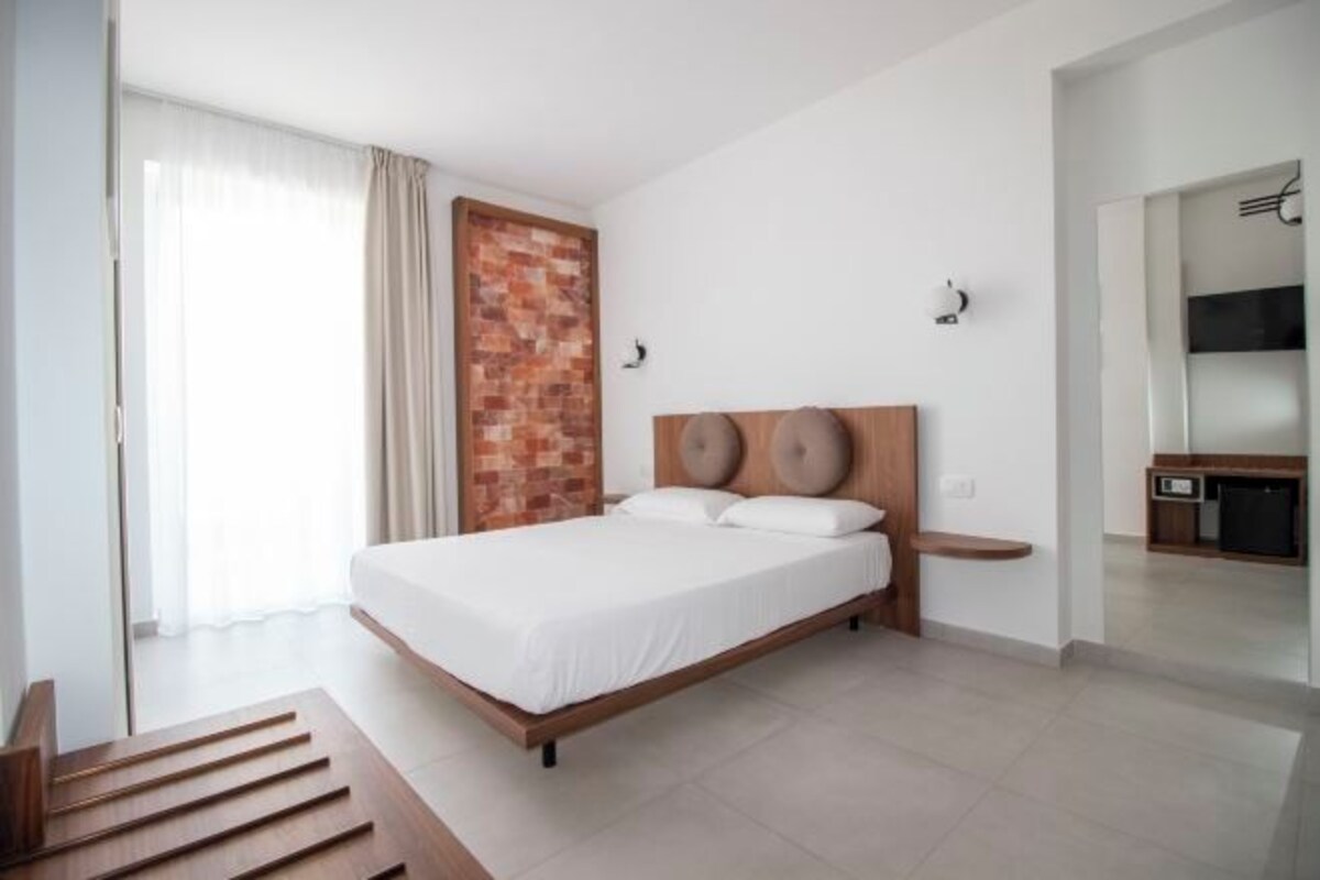 Una camera d'albergo moderna con un letto grande, una parete decorata in mattoni, un angolo cottura e una porta scorrevole in vetro.