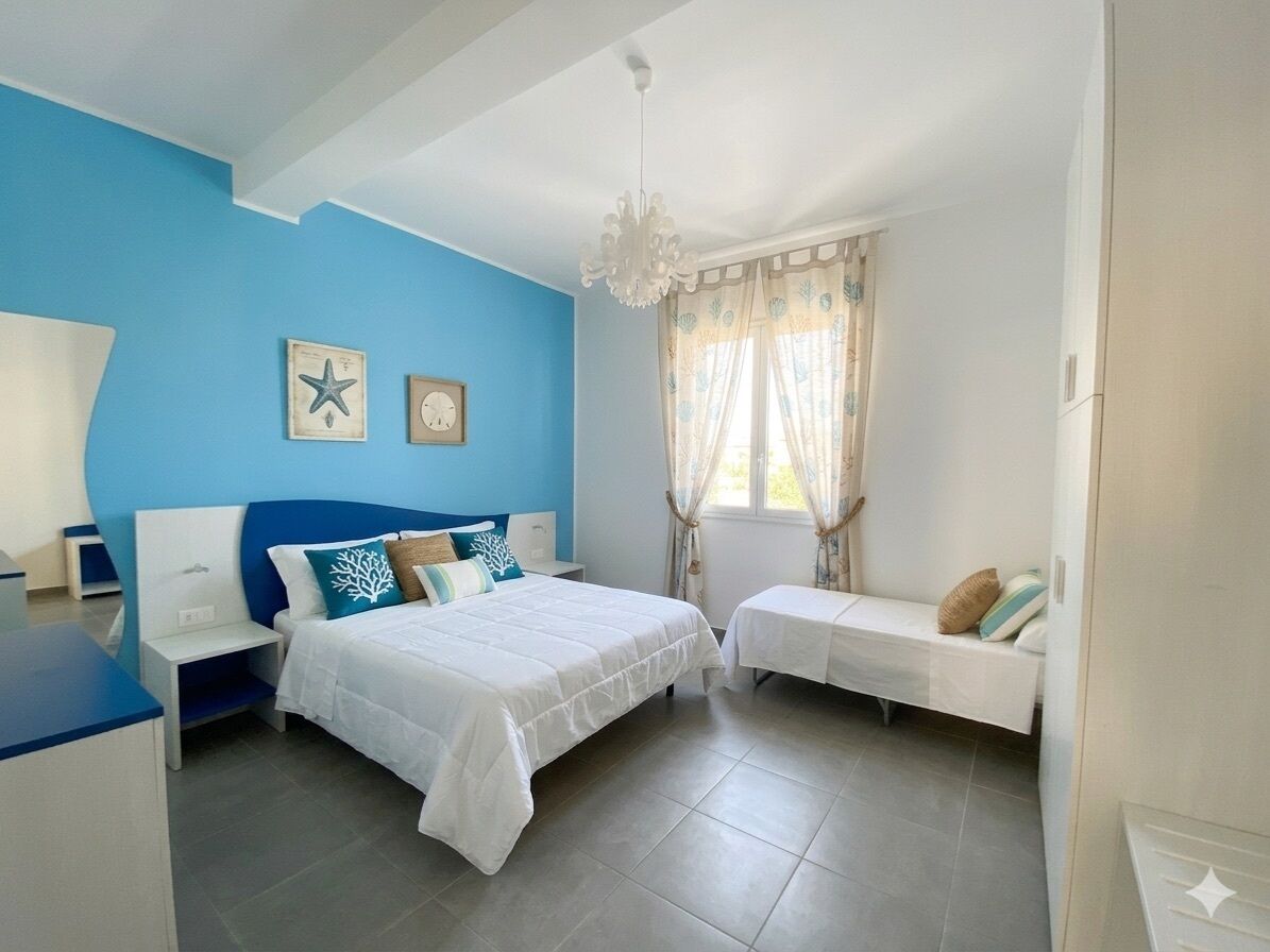 A bedroom with a bed, bedside tables, a nightstand, a chair, a window with curtains, and wall decorations.