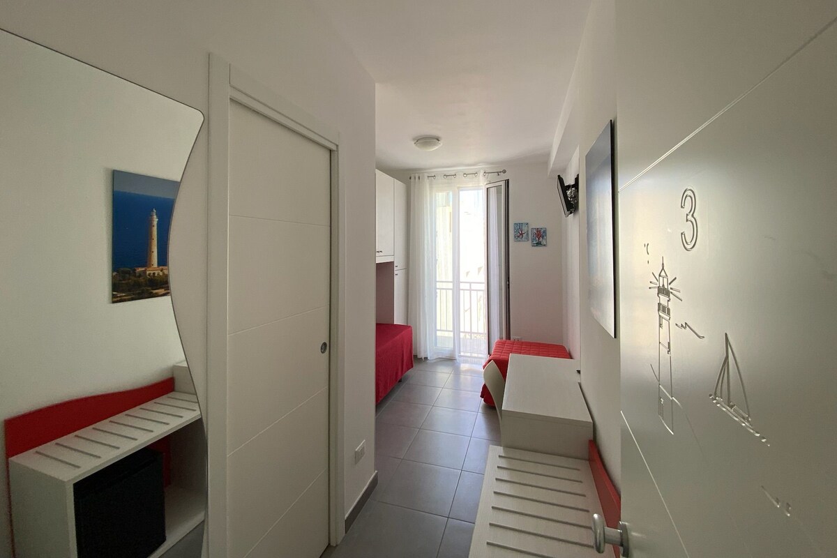 A hallway with a bed, a door, a window, and a wall with a number.