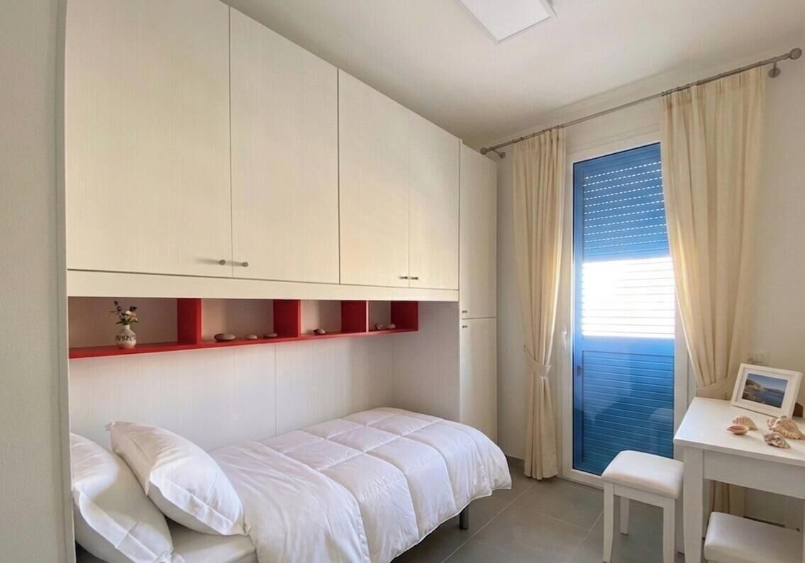 A bedroom with a bed, a desk, and a window with curtains.