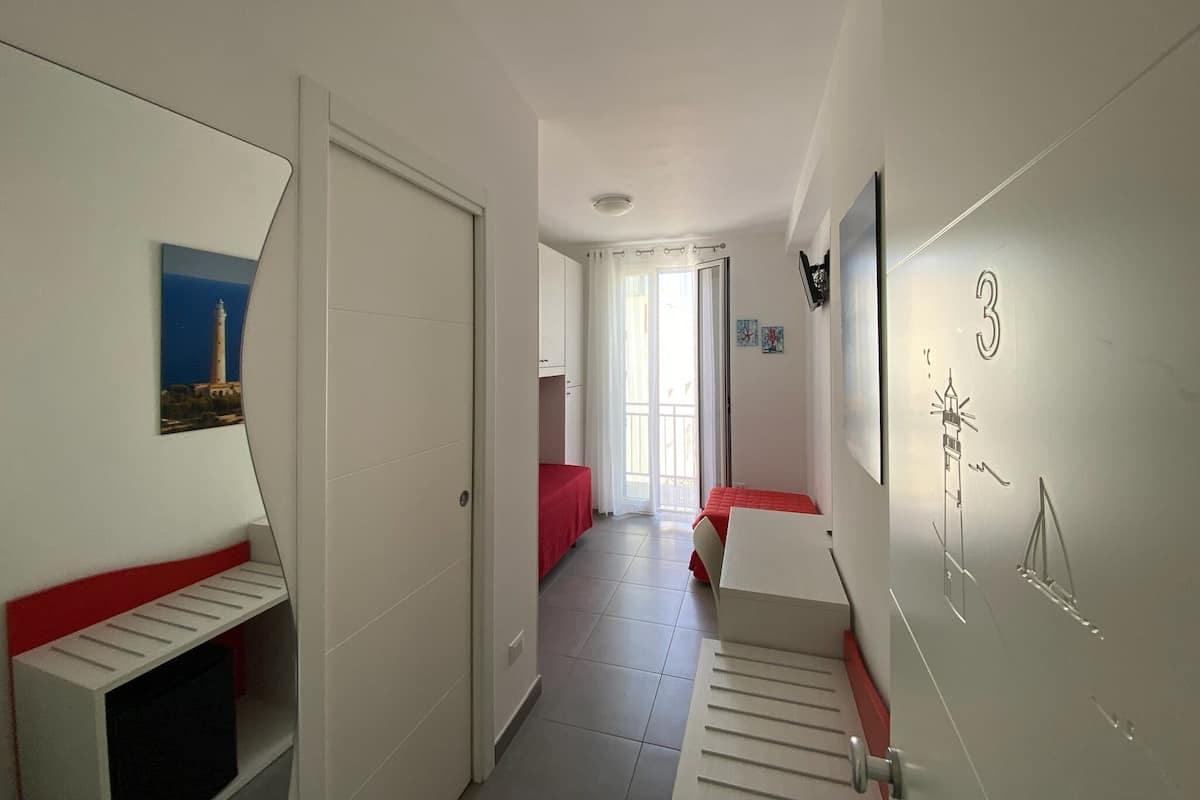 Un pasillo con una cama, una puerta, un ventanal y una pared con un número.