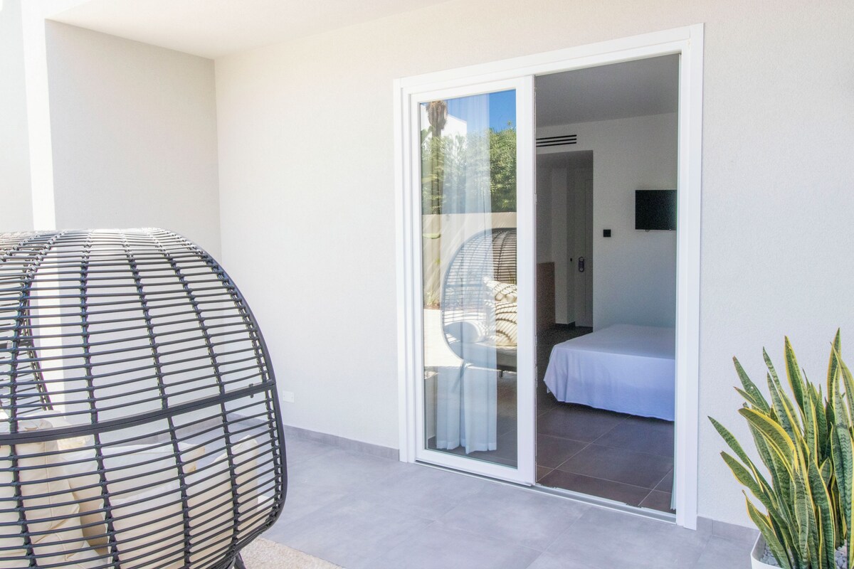 A modern room with a bed, a glass door leading to a balcony, and a potted plant.