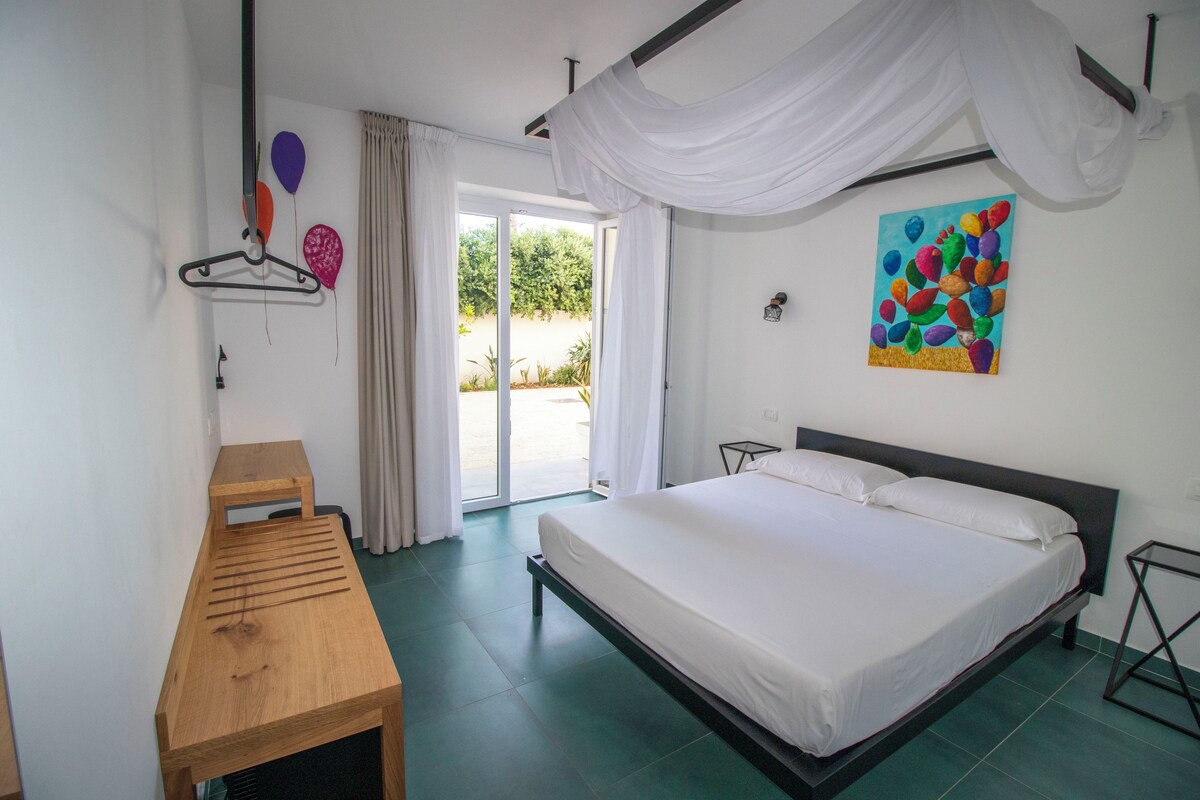 Een slaapkamer met een bed, een houten tafel, een schilderij en uitzicht door de deur.