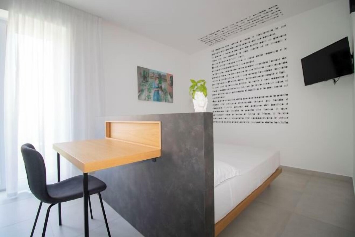 A modern room with a bed, a desk, a chair, a flat-screen TV, and a wall with text.