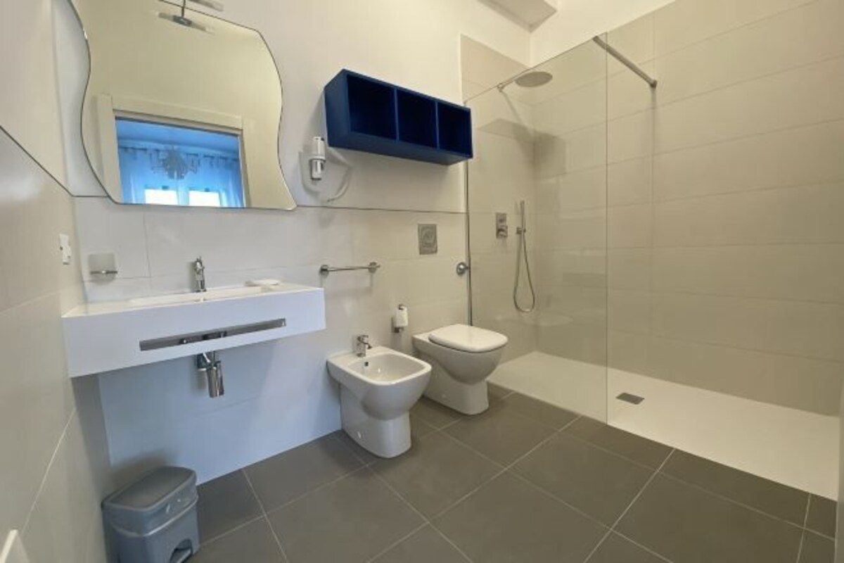 Un bagno moderno con doccia, WC, bidet e un mobile lavabo con specchio e lavandino.