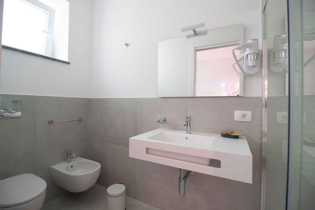 A modern bathroom with a pedestal sink, a bidet, and a glass shower enclosure.