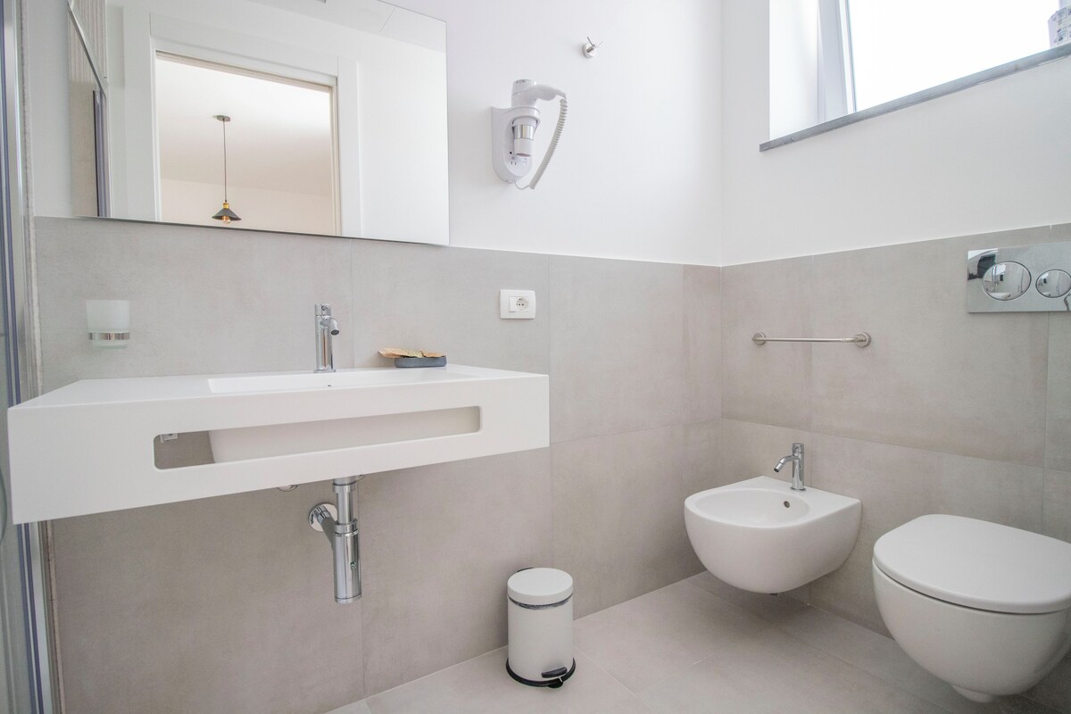 A modern bathroom with a white sink, bidet, and toilet.