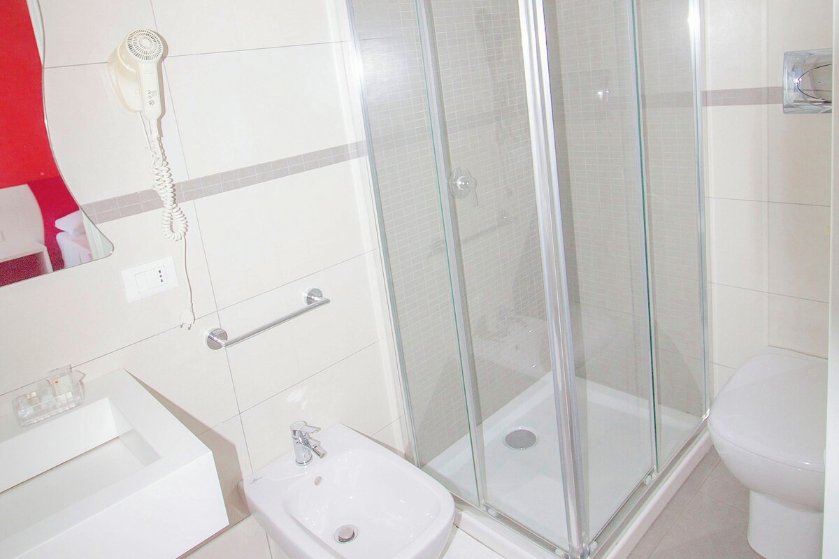 A bathroom with a glass-enclosed shower, a white bidet, and a white toilet.