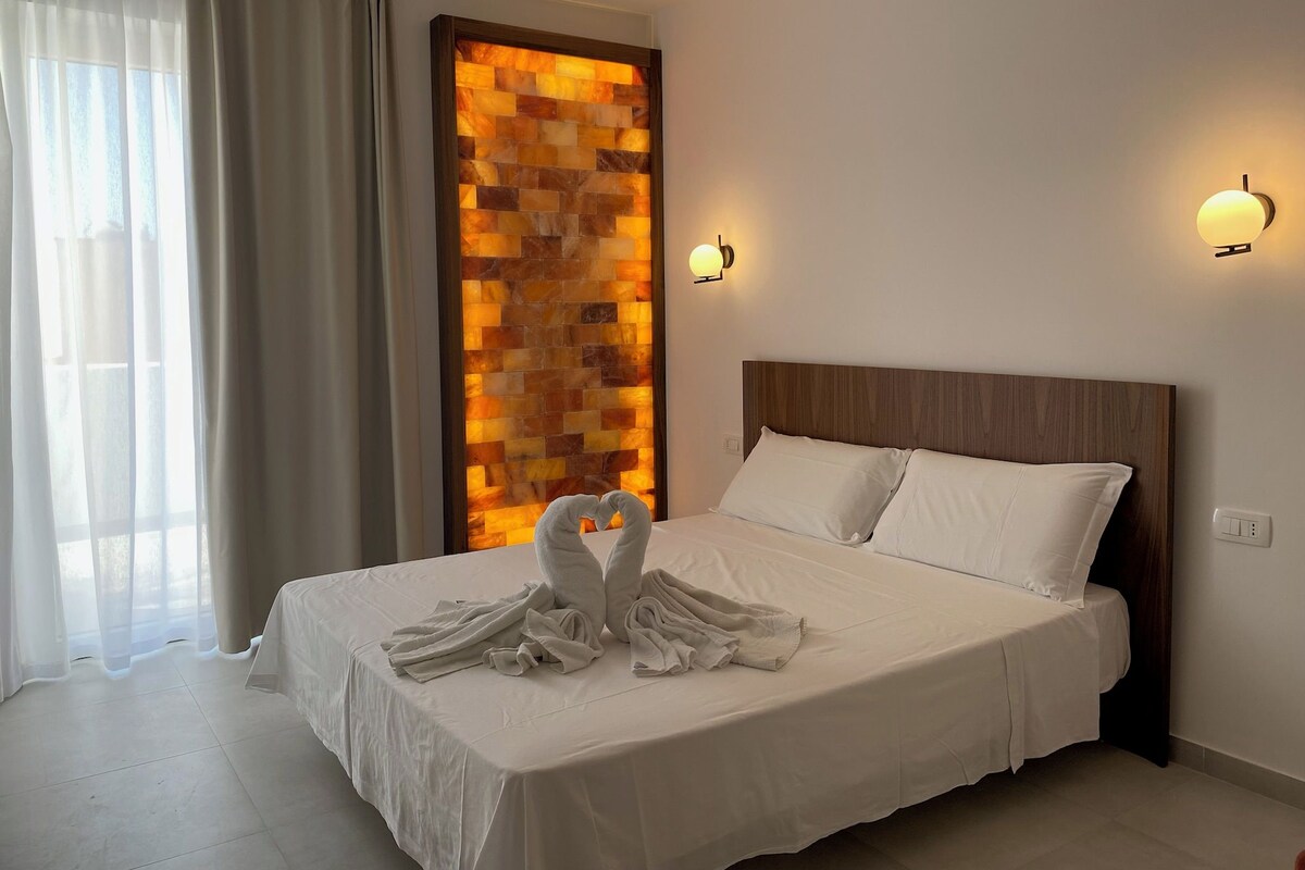 Een hotelkamer met een groot bed, een wandlamp en een decoratief paneel.
