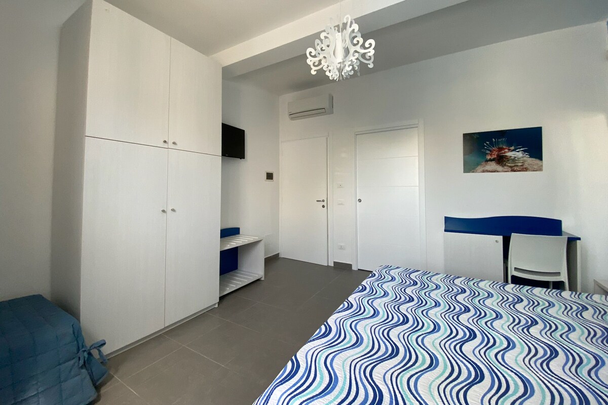 A bedroom with a bed, wardrobe, desk, chair, and a chandelier.