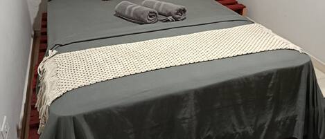 A single bed with a grey bedspread, a patterned pillow, and a white throw.