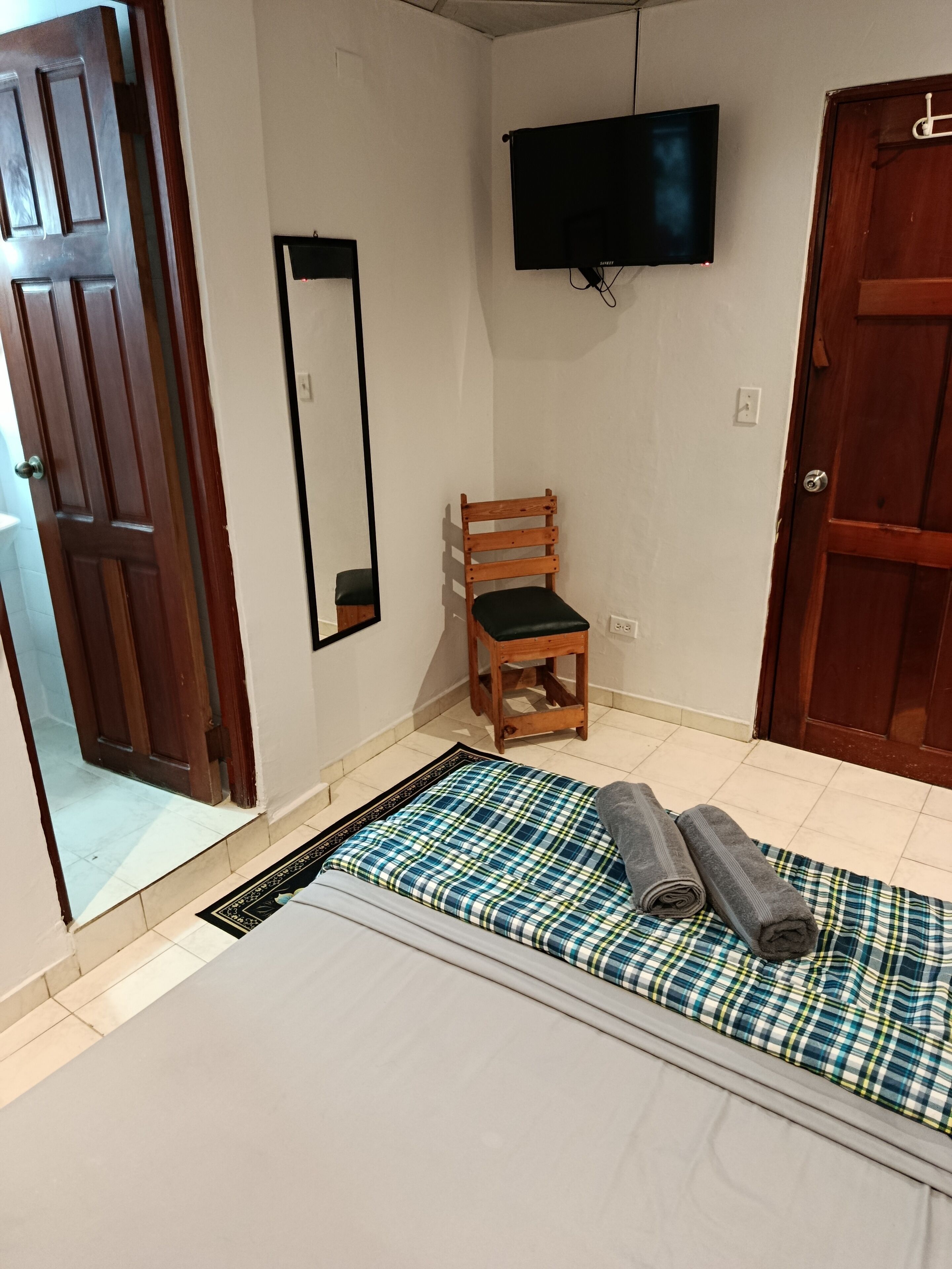 Une pièce comprenant un lit, une chaise en bois, un téléviseur fixé au mur et une porte.