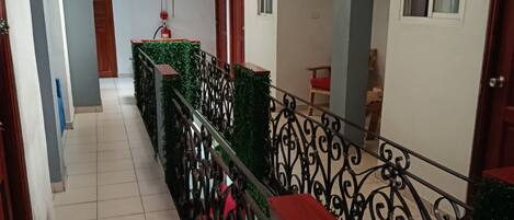 A corridor with a tiled floor, a metal railing, and a green plant wall.