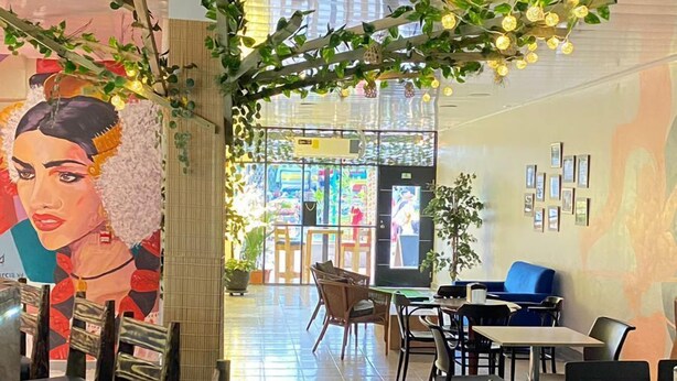 Un restaurante con una barra larga, sillas y mesas. Hay plantas e iluminación decorando el espacio.