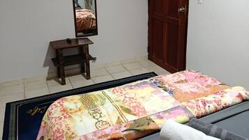 A bedroom with a bed, a wooden door, a small table, a mirror, and a television mounted on the wall.
