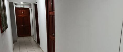A narrow hallway with tiled flooring, white walls, and wooden doors.