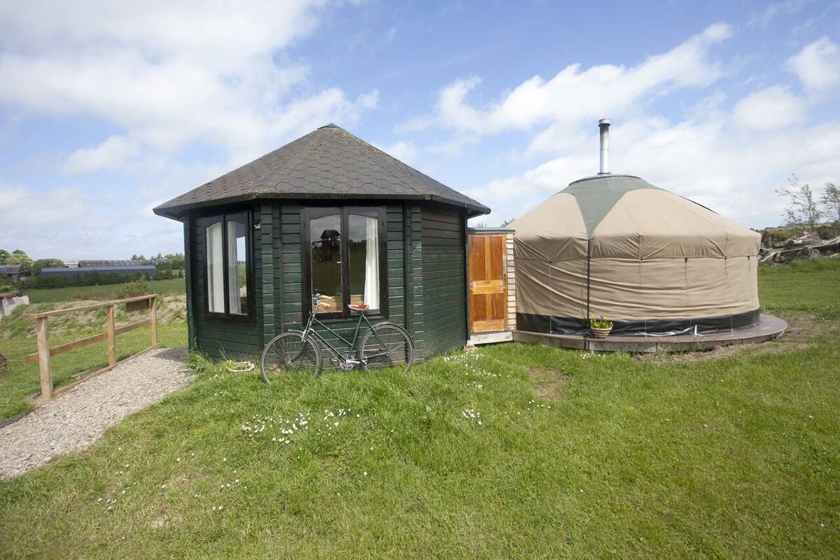 A small wooden cabin with a bicycle parked in front and a covered structure nearby.
