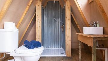 A small, rustic bathroom with a wooden floor, a white toilet, a sink, and a shower area.