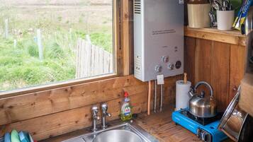 A compact kitchen with a built-in water heater, a sink, and a window overlooking a grassy field.