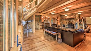 Ein Blockhaus-Interieur mit Kamin aus Stein, einer Holztreppe und einer gemütlichen Sitzecke.