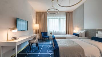A hotel room with two beds, a desk, a chair, a TV, and a large window with curtains.