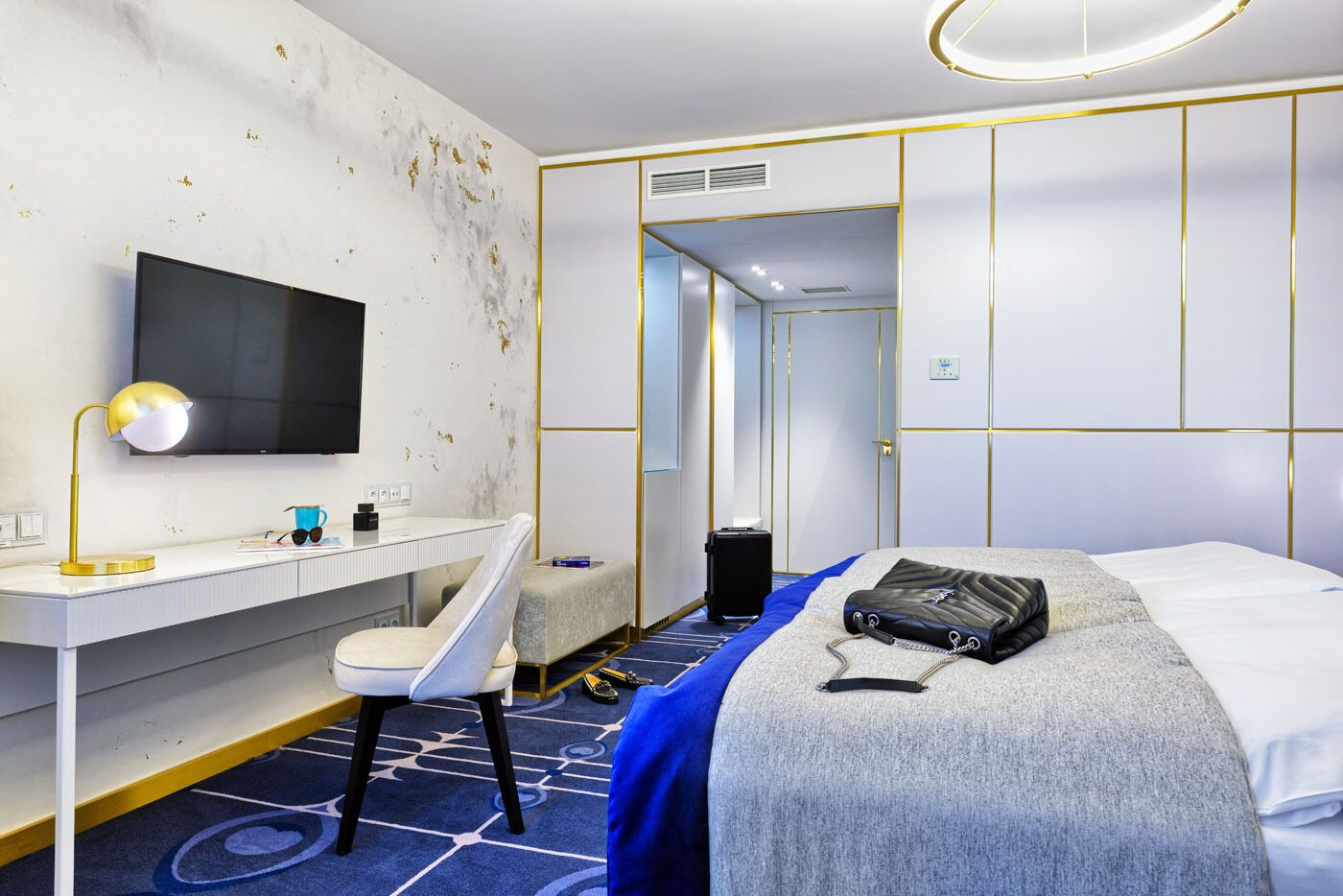 A hotel room with a desk, chair, bed, and a television.