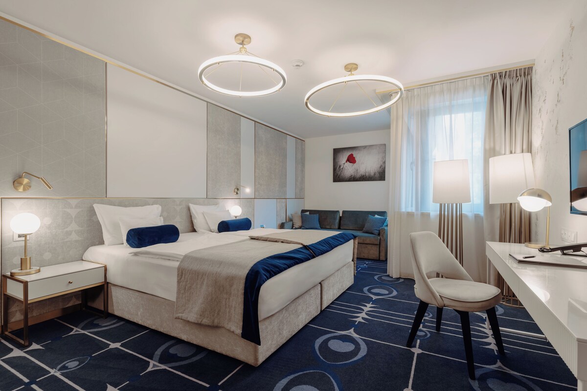 A hotel room with a large bed, a desk, a chair, a mirror, and a painting on the wall.